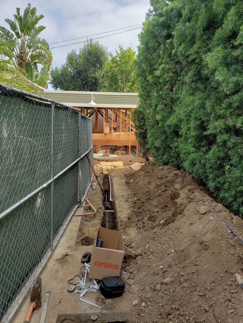 drainage-service-sewer-trench-replacement-orange-county New black ABS drain line installed in a trench along a chain-link fence at a job site