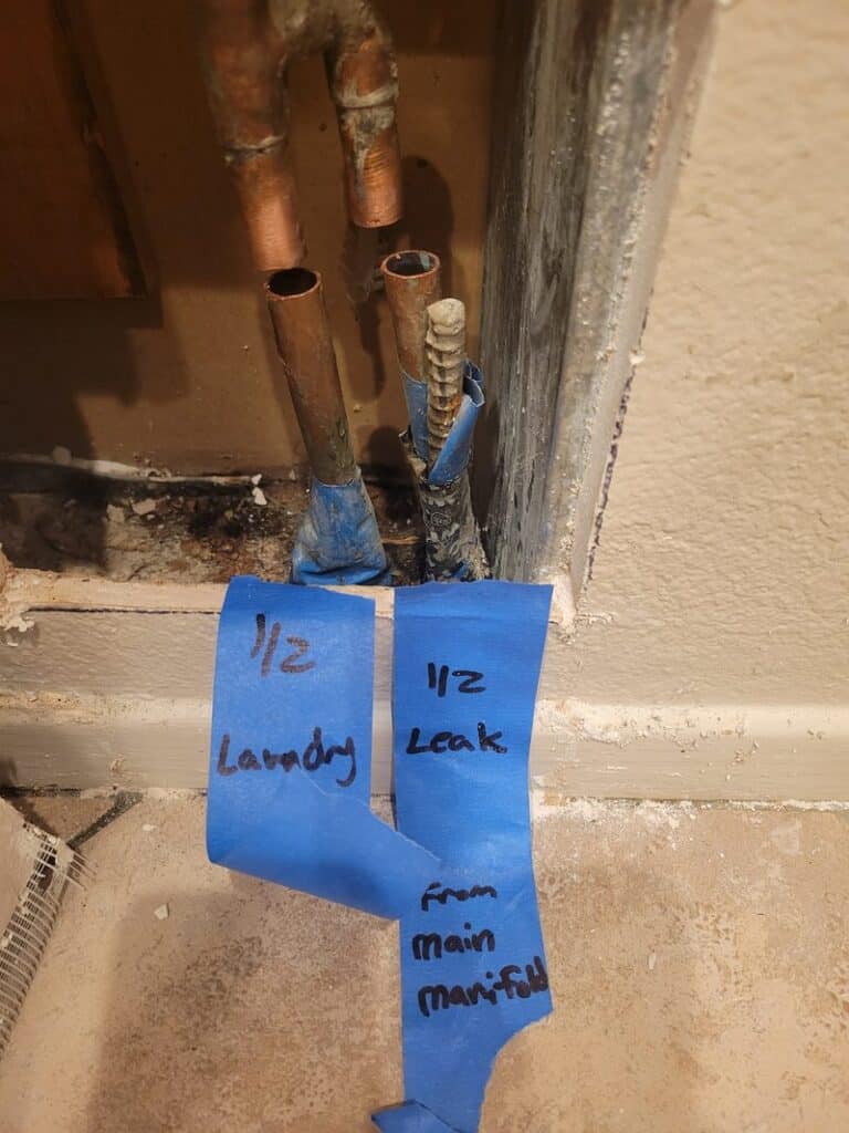 slab-leak-diagnostic-tape-labels-orange-county Slab leak diagnosis in Orange County: cut copper supply lines tagged "1/2 laundry" and "1/2 leak from main manifold" to isolate the leaking line
