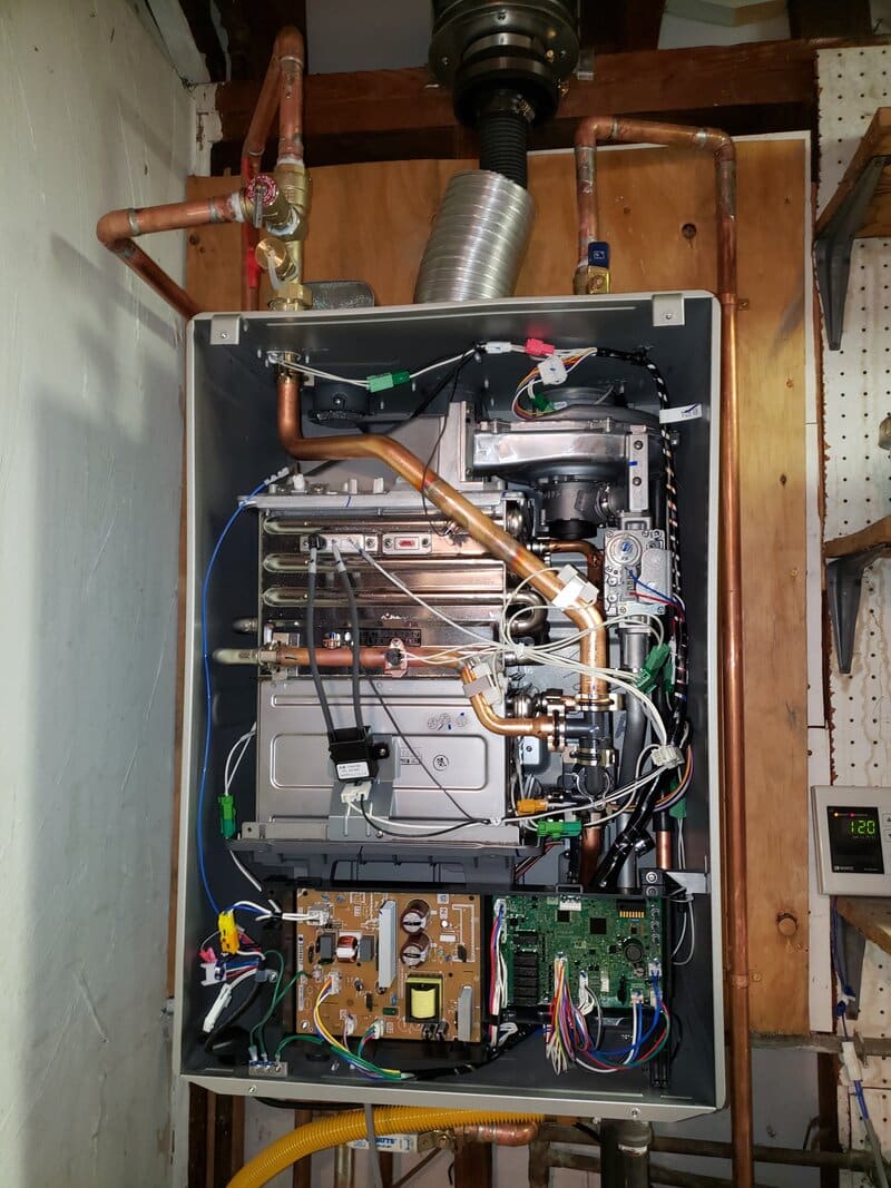 tankless-heat-exchanger-huntington-beach-orange-county A tankless water heater with the cover off at a Huntington Beach home, showing the heat exchanger and gas connections.